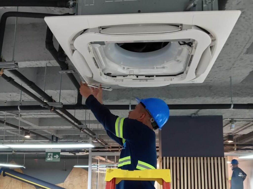 Técnico instalando unidad de aire acondicionado tipo cassette.