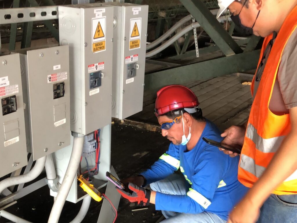 Técnicos instalando sistema de protección eléctrica para aire acondicionado comercial.